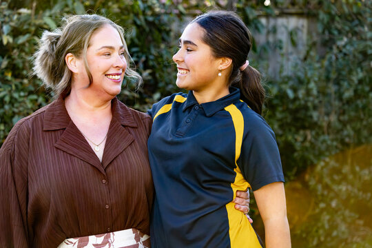 Mother's arm around tween daughter's waist standing in the garden looking at each other