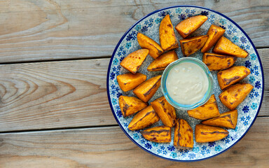 Top view of baked sweet potatoes on a platter and tahini dip in small bowl. Rustic wooden background with space for text or logo.