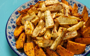 Baked root vegetables with thyme: parsnip and sweet potatoes. Blue background. Healthy vegetarian food.
