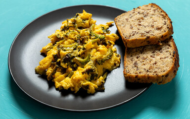 Stir-fried bitter melon eggs on a black plate with two pieces of bread. Blue background.