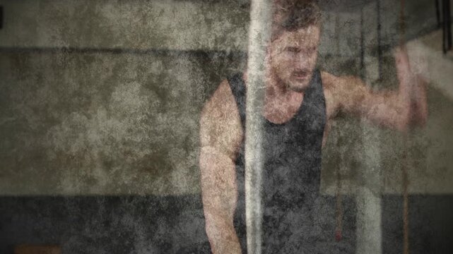 Man gripping battle rope, making alternating waves in fitness gym while grunge layer for strength