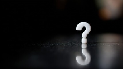 Close-up of a white question mark on a black surface. the question mark is in the center of the image and is slightly tilted to the right.