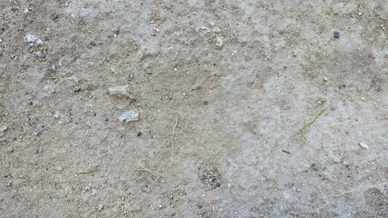 Rough ground texture with small gravel, sand, and a few green grass blades. Ideal background for nature, construction, or outdoor design projects.