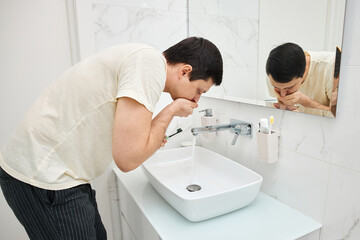 Man rinsing after brushing teeth over sink in modern bathroom