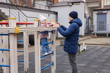 Caring father assisting his child on a playground monkey bars in winter season