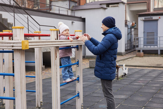 Caring father assisting his child on a playground monkey bars in winter season - Powered by Adobe