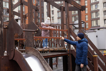 Caring dad assisting child enjoying outdoor play on urban playground in winter