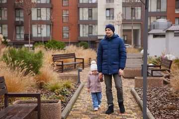 Father and young daughter walking together holding hands in a modern urban park