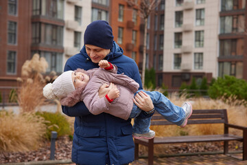 Father playing with happy daughter, having fun outdoors in warm winter clothing