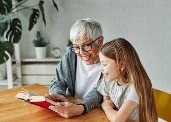 Portrait of grandmother and granddaughter having fun together reading a book at home