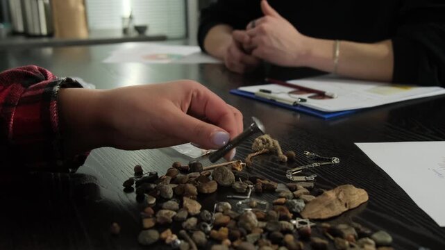 Woman dressed in shirt lays out small trinkets on table surface. Lady alternately takes things in hands showing bracs to audience
