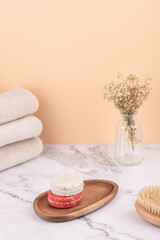 Vertical composition with natural solid shampoos on a wooden tray, beige towels, massage brush and vase with dried flowers. Peach background and marble surface. Copy space. Concept of self care