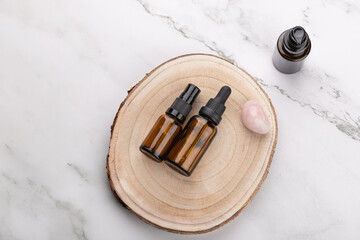Top view horizontal of two amber glass cosmetic bottles on wooden base with rose quartz stone on light marble background. Copy space. Concept of natural skincare and wellness