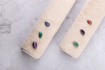 Horizontal flat lay of two beige towels with colorful decorative stones on light geometric stone surface. Spa and relaxing style. Copy space. Concept of holistic wellness and relaxation