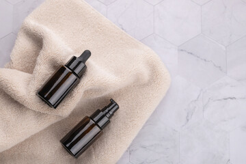 Horizontal flat lay of two dark brown cosmetic bottles on beige towel over gray stone surface. Natural and minimalist style. Copy space. Concept of wellness routine and natural beauty