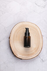 Vertical flat lay of amber cosmetic pump bottle on wooden base over light geometric stone background. Minimal natural style with copy space. Concept of organic skincare and wellness