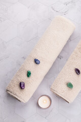 Vertical flat lay of two beige towels with colorful natural stones and lit candle on geometric stone background. Minimal and relaxing style. Copy space. Concept of cozy wellness and self care