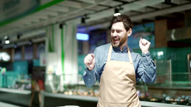 Happy cheerful male employee in a grocery store or supermarke dancing Funny man the seller dances in the meat department. Salesman worker staff seller having fun in food market