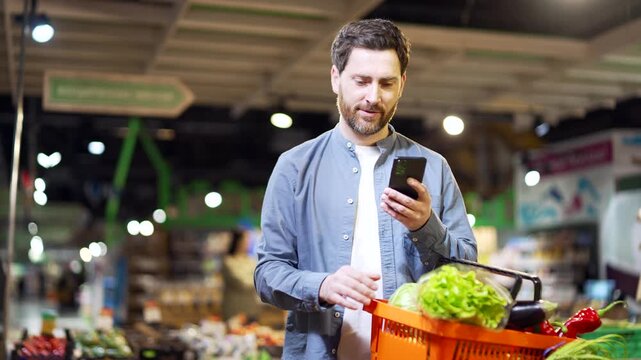 Man Buyer customer checking shopping list using browsing smartphone, purchasing in grocery store in supermarket Handsome male shopper pick use mobile phone in hypermarket or food market at shop 