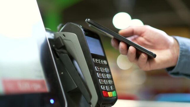 Close up man At Counter Buy electronic payment supermarket mall smartphone close-up male hand with mobile phone in hands pay paid for purchases in stores Contactless NFC Terminal Closeup card reader
