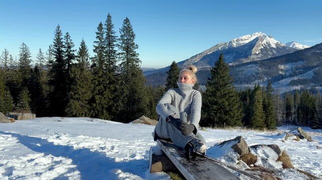 A woman with thermos and walking sticks in winter mountains