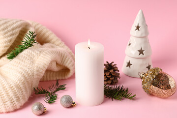 Burning candle with Christmas decor and sweater on pink background