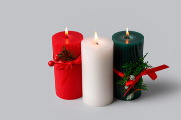 Burning candles with Christmas decor on light background