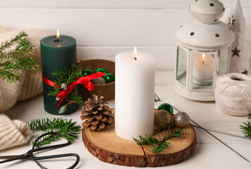 Burning candles with Christmas decor on white wooden table