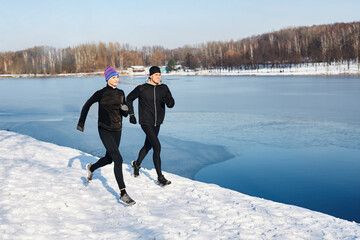 Couple running in winter - active joggers training together by lake in urban park