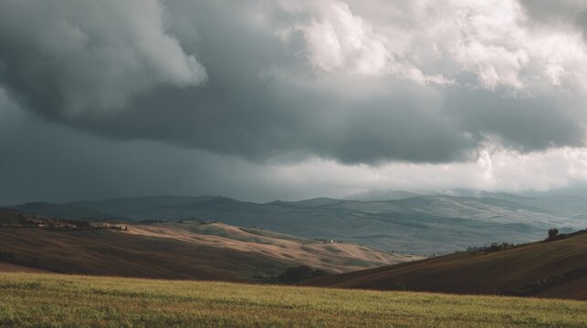 Landscape photograph of a vast open field with rolling hills in the background. the sky is filled with dark, ominous clouds that are covering most of the sky.