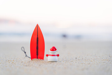 Sandy Christmas Snowman is watching the waves, standing on beautiful beach with a surf board - horizontal version in Patong Beach, Phuket, Thailand
