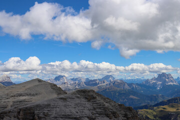 Fototapeta premium Dolomites Italy mountain panorama: aerial cliffs soaring under blue sky and cotton-like cumulus clouds