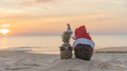 Santa Claus pineapple and watermelon couple wearing stylish sunglasses on the sand contrasting with the sea. wearing a christmas hat Christmas and New Year holiday ideas on the beach, Patong, Phuket