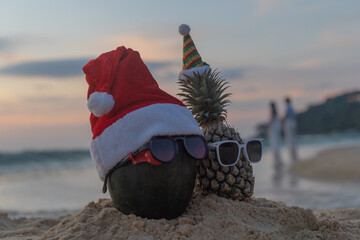 Santa Claus pineapple and watermelon couple wearing stylish sunglasses on the sand contrasting with the sea. wearing a christmas hat Christmas and New Year holiday ideas on the beach, Patong, Phuket