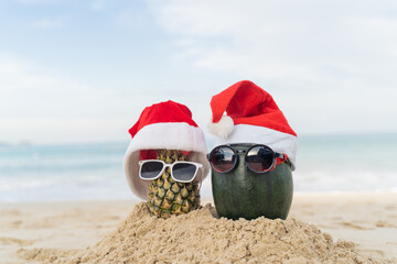 Santa Claus pineapple and watermelon couple wearing stylish sunglasses on the sand contrasting with the sea. wearing a christmas hat Christmas and New Year holiday ideas on the beach, Patong, Phuket