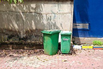 Obraz premium Two Green Outdoor Trash Bins Stand Next To A Textured Wall And Blue Structure