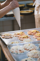 Cook puts the sauce on the mini pizza in the bakery