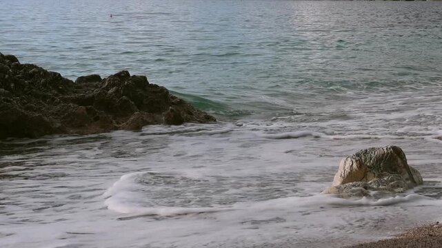 Seascape with sandy shore and rock, waves rolling gently on summer coast in tranquil ocean scenery