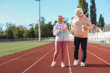Sporty senior couple with water bottles training at stadium