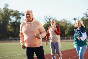 Obraz premium Sporty senior man with group running at stadium