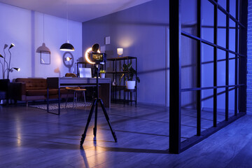 Interior of dark blogger's room with workplace, camera and glowing lamps