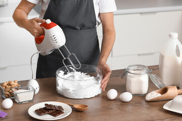 Woman whipping egg albumen with mixer in kitchen