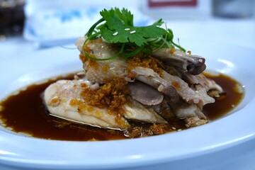 Tender Chinese steamed chicken served with rich soy-based sauce, topped with fried garlic, fresh cilantro, and sliced green onions for garnish.