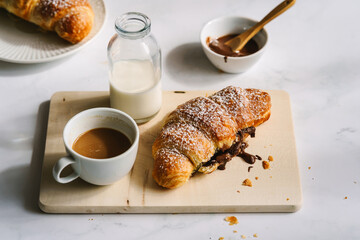 Gebackenes Schokolade Croissant und eine Tasse Kaffee auf einem wei&szlig;en Tisch. Franz&ouml;sisches Fr&uuml;hst&uuml;ck, Dessert.