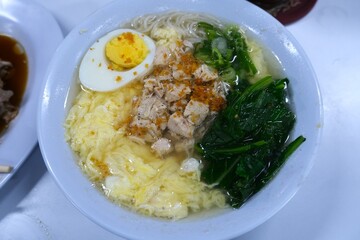 Warm bowl of Indonesian misoa noodle soup served with shredded chicken, boiled egg, vegetables, and flavorful clear broth.
