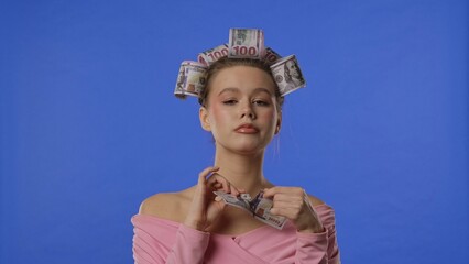 A woman with curlers wrapped in money tears a banknote