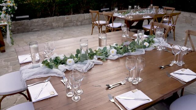 Tables are beautifully arranged outdoors with elegant decorations. Glassware and table settings create a perfect atmosphere for a special gathering in a serene garden.