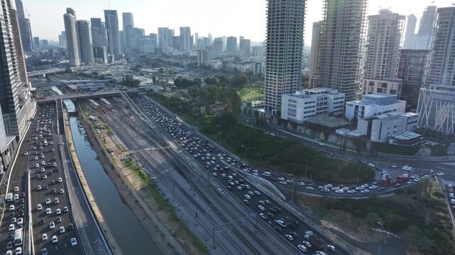 Aerial drone shot of the Ayalon Highway in Tel Aviv, featuring the central railway tracks, the Ayalon river canal, and busy traffic flowing between modern high-rise buildings.