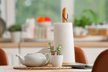 Roll of paper towels with tea set and plant on dining table in kitchen, closeup