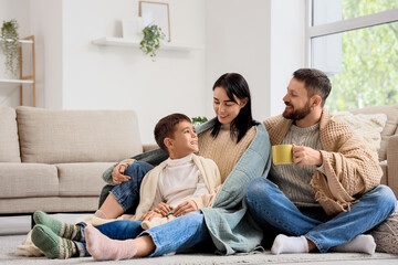 Obraz premium Happy parents and their little son with warm plaids sitting at home
